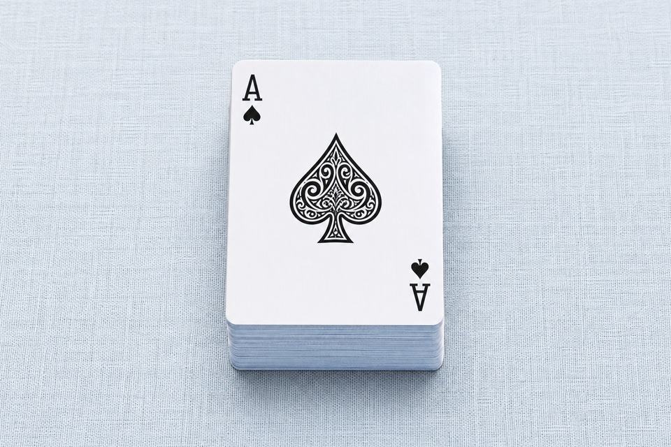 浅蓝亚麻桌布上整齐叠放的一副扑克牌，最上方是黑桃A
